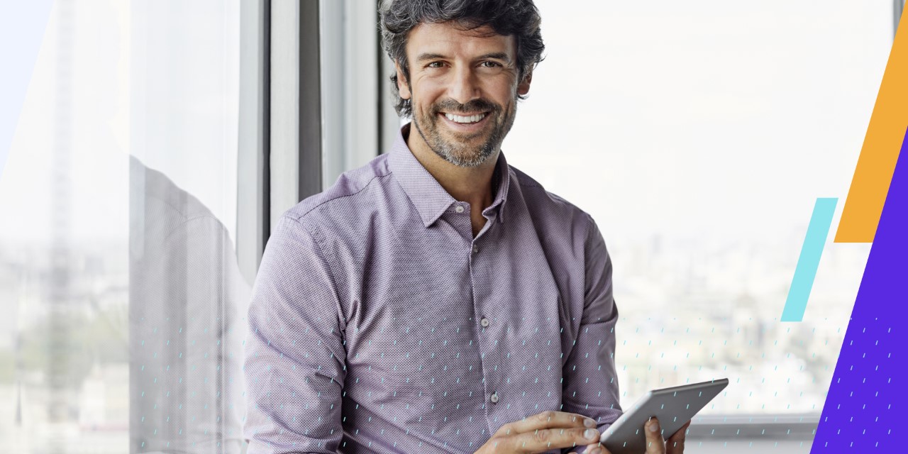 a happy man works on a tablet and looks at the viewer